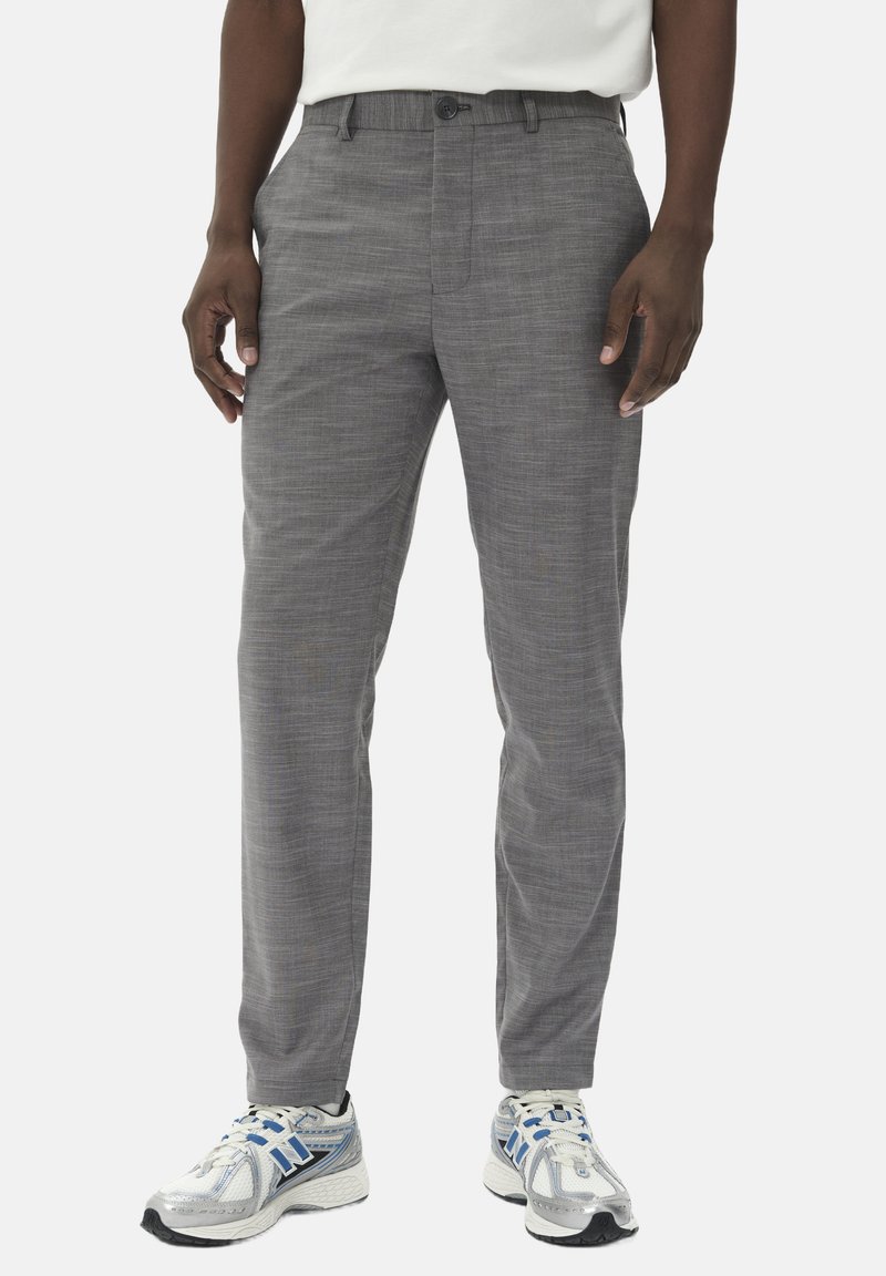 Pantalons gris fuselés en tissu texturé, avec une fermeture à un bouton et des poches latérales, portés avec des baskets de sport.
