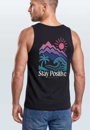Mann, seitlich gewandt, trägt ein schwarzes Tanktop mit bunten Bergen, Sonne, Palme, Welle und dem Schriftzug „Stay Positive“ auf dem Rücken.