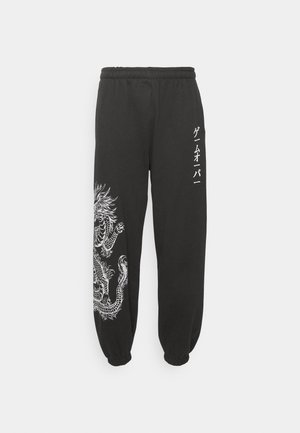 Sorte sweatpants med elastisk talje og manchetter, der har et stort hvidt dragegrafik på den ene side og japansk tekst på den anden.