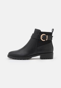 Bota de cuero negro hasta el tobillo con punta redonda, paneles laterales elásticos y un detalle en hebilla dorada. Tacón bajo resistente y suela texturizada.