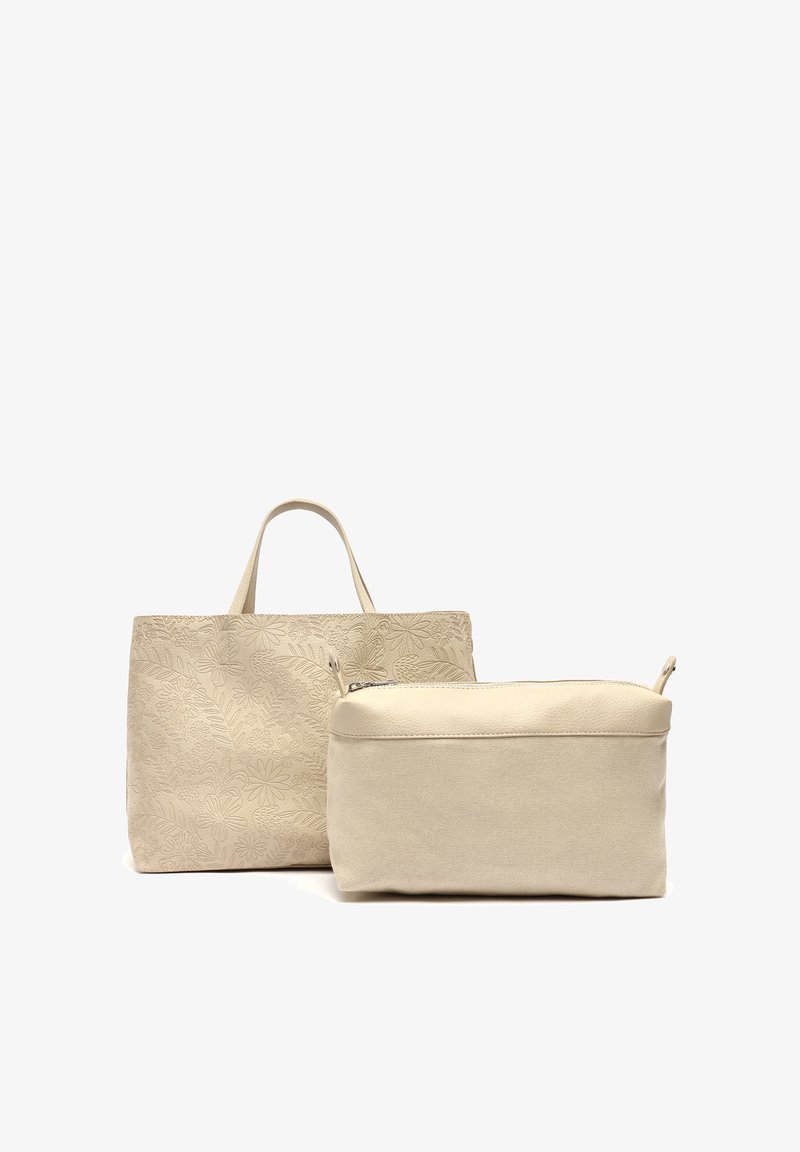 Vaaleanbeige kangaskassi, jossa on kukkakuosisia kohokuvioita ja lyhyet kahvat, yhdistettynä pienempään, kermaiseen vetoketjulliseen pussiin. Molemmilla on sileä pinta.