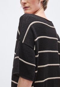 Μπλούζα με κοντά μανίκια σε μαύρο χρώμα με λευκές οριζόντιες ρίγες, υφή υφάσματος, φαρδιά λαιμόκοψη και άνετη εφαρμογή, που αναδεικνύει έναν χαλαρό σχεδιασμό.