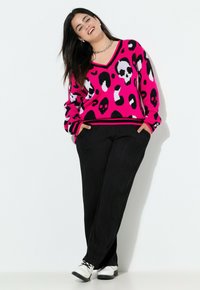 Maglione oversize rosa con motivo di teschi in bianco e nero, abbinato a pantaloni larghi a coste neri e scarpe bianche. Design e texture casual.