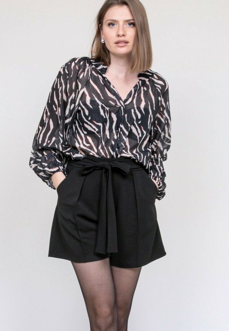 Shorts noirs avec une taille à nouer et un blouse transparent à manches longues présentant un motif animalier rose et noir.