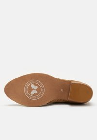 Semelle de chaussure marron et texturée avec un logo circulaire représentant deux feuilles. Taille 37 imprimée près du talon.