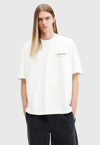 White oversized cotton t-shirt with short sleeves, featuring a small gray "ALLSAINTS" logo on the left chest area. Smooth texture.