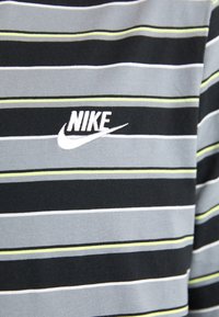 Juodas ir pilkas dryžuotas marškinėliai su žaliai gelsvais ir baltais akcentais. Ant krūtinės yra siuvinėtas Nike logotipas. Pagaminti iš minkštos medvilnės medžiagos.