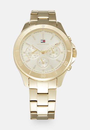 Montre en acier inoxydable doré avec un cadran rond, trois sous-cadrans et un bracelet lisse à maillons. Présente des index numériques et un logo à 12 heures.