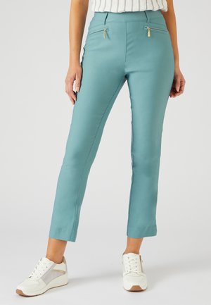 Teal broek met een aansluitend ontwerp, voorzien van twee ritszakken aan de voorkant, in combinatie met witte sneakers. Soepele textuur, cropped lengte.