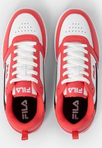White and red athletic sneakers with textured leather, lace-up design, perforated toe, and visible logo on the tongue and side.