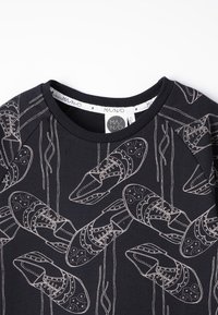 Felpa nera con un motivo ripetitivo di scarpe contornate in beige, con lacci dettagliati e accenti decorativi. Collo a costine.