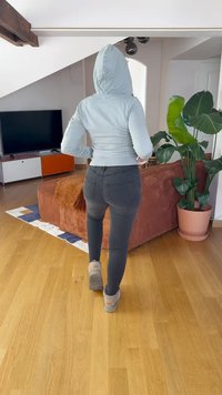 Svijetloplava dukserica s kapuljačom, uske crne traperice i sivi tenisice. Unutarnji prostor s drvenim podom i zelenom biljkom u loncu.