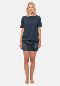 Donkerblauwe katoenen t-shirt met korte mouwen, gecombineerd met zwarte gestreepte shorts. De shorts hebben een relaxte pasvorm en een lengte tot halverwege de dijen.