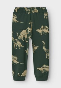 Tamsiai žali vaikų kelnės su kremiškos spalvos dinozaurų raštais, įskaitant T-Rex, Stegosaurus, Brachiosaurus ir Spinosaurus, su elastinga juosta ir kulkšnies apvadu.
