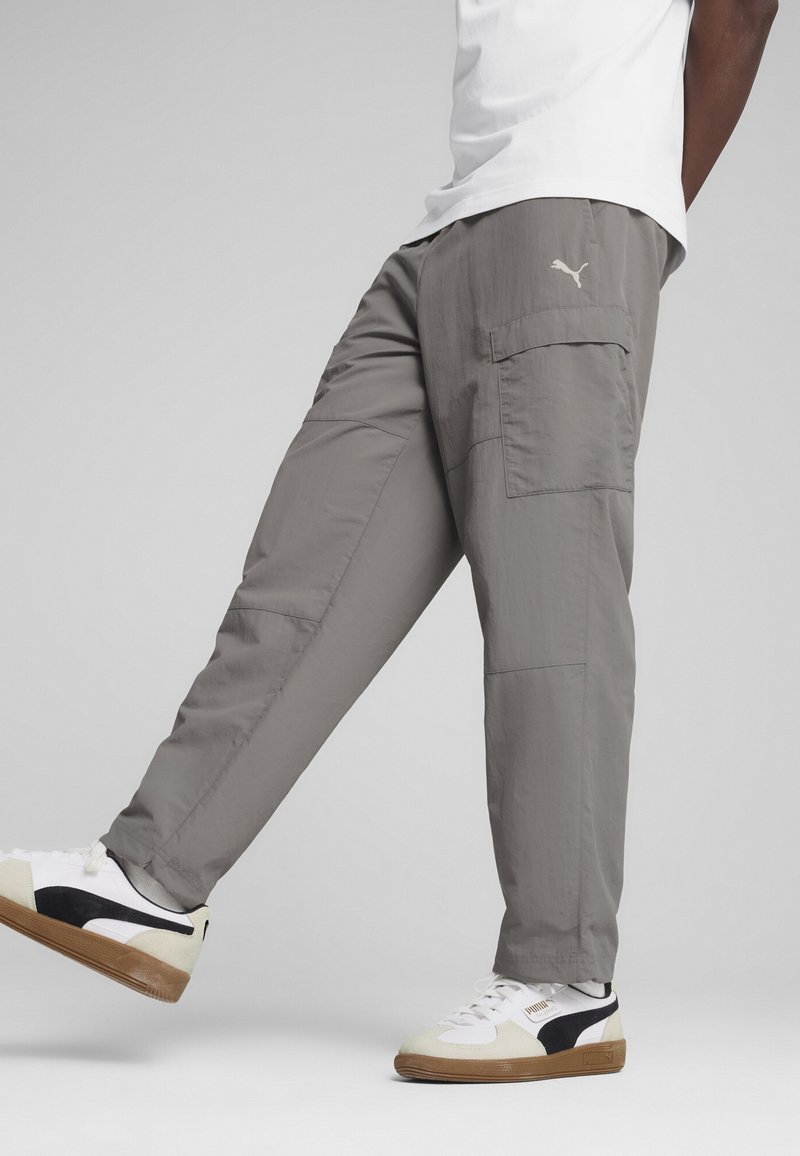Grå cargo bukser med lommer, tapered design og let materiale, parret med hvide sneakers med sorte accenter og gummisåler.