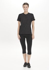 Zwart sporttop met korte mouwen van textuurstof, gecombineerd met zwarte capri legging met een decoratieve rand en fietsschoenen.