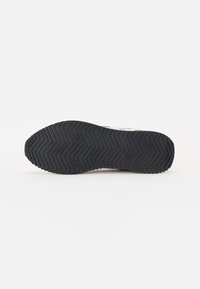 Sola nera di scarpa da ginnastica con un motivo a spina di pesce, caratterizzata da un bordo liscio e una leggera usura. Materiale in gomma durevole con una texture sottile.