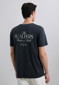 Camiseta de algodón gris oscuro de mangas cortas, con texto blanco en la parte posterior que incluye "The SCALPERS" y los detalles del evento.