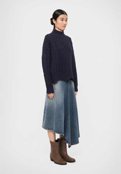 Navy knitted sweater with a high neck, light blue asymmetric denim skirt, and brown ankle boots with a slight heel.