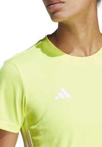 Camiseta deportiva amarilla con cuello redondo, que presenta detalles de acentos de malla en los hombros y un logo blanco de Adidas en el pecho.