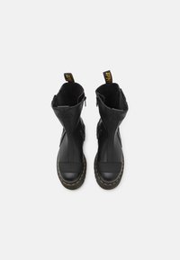 Black leather ankle boots with a textured finish, yellow stitching along the sole, and rear pull tabs for easy wear. Zipper closure along sides.
