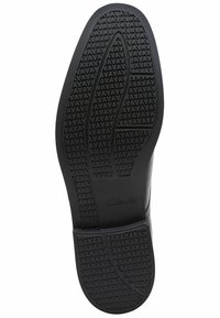 Sole di sneakers nera con grip in gomma testurizzata. Presenta un modello pronunciato per la trazione e una suola intermedia liscia. Marchiata "Clarks."