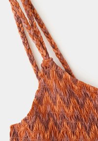 Detailní záběr oranžové a hnědé texturované látky s třemi pletenými popruhy, zobrazující detailní šití a nashromážděný materiál.