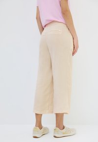 Beige wide-leg pants made of textured fabric, featuring a back pocket and cropped length, paired with light-colored sneakers.