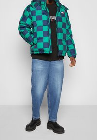 Green and navy checkered puffer jacket with a hood, worn over a black sweatshirt, paired with light blue jeans and black chunky boots.