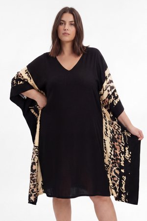 Femme portant une robe noire ample avec des panneaux beige et imprimé léopard comportant un texte en écriture cursive, debout avec une main sur la hanche et l’autre tirant le côté de la robe.