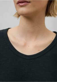 Tmavozelený top s okrúhlym výstrihom, s rebrovanou textúrou a viditeľným šitím. Detailný pohľad na oblasť krku a goliera.