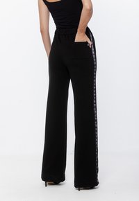 Czarne dresowe spodnie z prostą nogawką, elastycznym paskiem w talii i tylną kieszenią. Posiadają boczne paski z powtarzającym się małym wzorem.