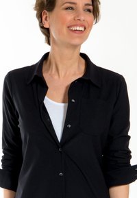 Zwarte button-up shirt met een kraag, voorzien van één borstzak, gemaakt van een gladde stof. Lange mouwen zijn opgerold.