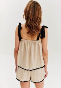 béžová ľanová trojdielna súprava pohodlného oblečenia s čiernymi volánovými akcentmi, obsahujúca voľný top s viazacím popruhom a zodpovedajúce šortky.