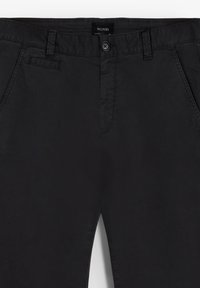 Pantalones negros ajustados con una textura suave, que cuentan con cierre de botón, bolsillos frontales y un diseño de cintura limpio.