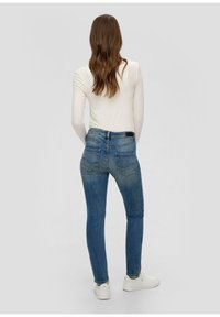 Skinny jeans in medium blue denim, featuring a high waist, two back pockets, and a subtle faded finish. Worn with a white long-sleeve top.