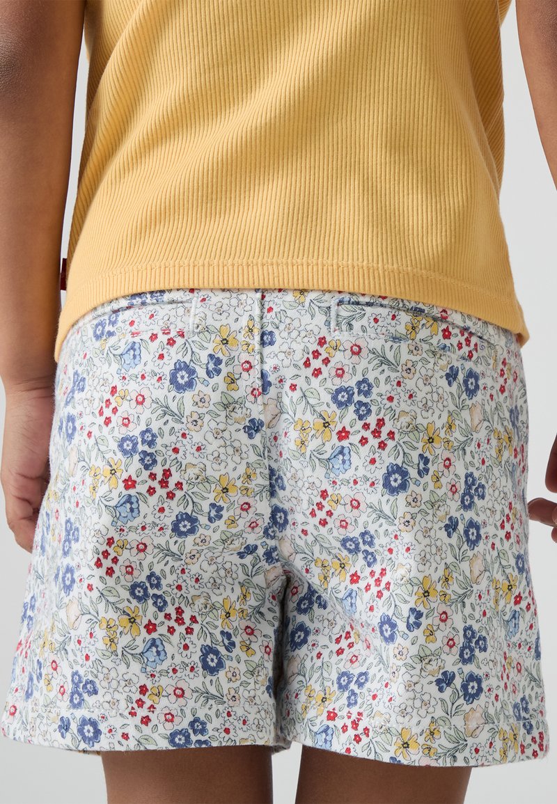 Shorts fleuris en tissu léger avec un fond blanc, ornés de fleurs bleues, rouges et jaunes ; design simple, sans poches visibles.