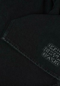 Pantaloni in denim neri con una texture liscia, caratterizzati da una stampa logo unica nell'area coscia. Le cuciture sono visibili lungo i bordi.