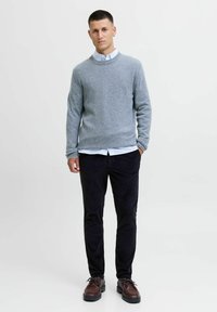 Szary sweter dzianinowy na białej koszuli z kołnierzykiem, w połączeniu z czarnymi spodniami z kordurowej tkaniny i brązowymi butami sznurowanymi. Minimalistyczny design, średni krój.