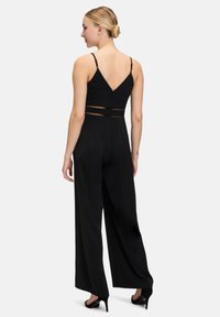 Zwarte jumpsuit met een V-achterdesign, verstelbare bandjes, een meshpaneel bij de taille en wijde broekspijpen. Soepele stoftextuur.