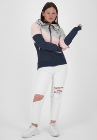Felpa con zip color block in grigio, rosa e blu navy con cappuccio. Abbinata a jeans bianchi strappati e sneakers bianche.