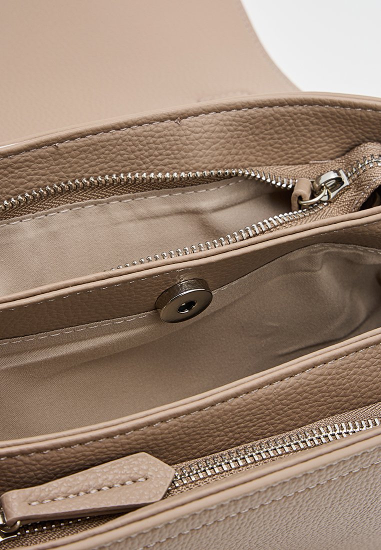 Intérieur d'un sac à main en cuir texturé beige avec deux compartiments, doublure en tissu beige, une fermeture éclair et un détail de fermeture magnétique.