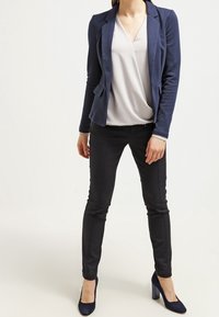 Blazer bleu marine ajusté porté sur un chemisier clair, associé à un pantalon noir slim et des escarpins bleu marine, créant un look professionnel.