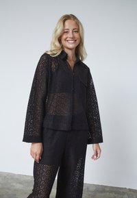 Sort blonde outfit bestående af en button-up skjorte med lange ærmer og et matchende par bukser, der fremviser et geometrisk udsnit mønster.