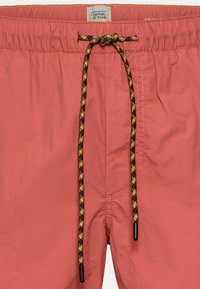 Licht koraalkleurige zwembroek met een elastische tailleband, zwarte en gele trekkoord, en zijzak. Gemaakt van lichtgewicht materiaal.