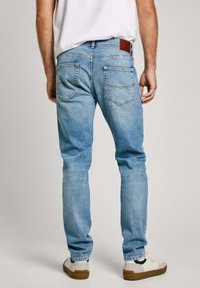 Heledad sinine denim jeans sirge lõikega, millel on kaks tagataskut, nähtav õmblus ja pruun nahkplaat vööl.