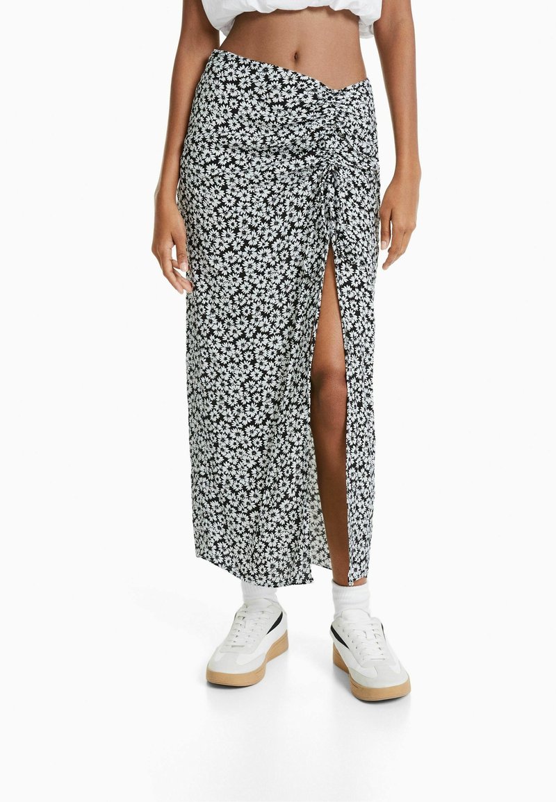 Schwarz-weißer Floral-Maxi-Rock mit einem seitlichen Schlitz und Raffung an der Taille, kombiniert mit weißen Sneakers. Glatte Stofftextur.
