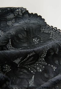 Black lace fabric with floral patterns and scalloped edges in close-up view on a plain light background.