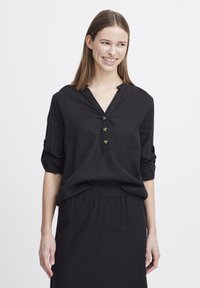 Blusa di lino nera con scollatura a V, tre bottoni e maniche arrotolate, abbinata a una gonna con vita elasticizzata coordinata. Texture liscia.