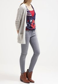 Ljust grått, strukturerat cardigan över en marinblå blommig topp, matchat med figurnära ljusgrå jeans och bruna ankelboots med låg klack.
